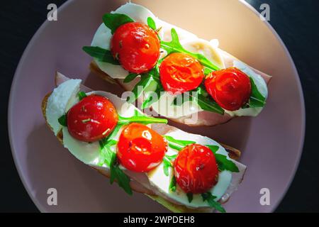 Sandwich con prosciutto, mozzarella, rucola e pomodori ciliegini. Vista dall'alto, sfondo in pietra nera. Foto Stock