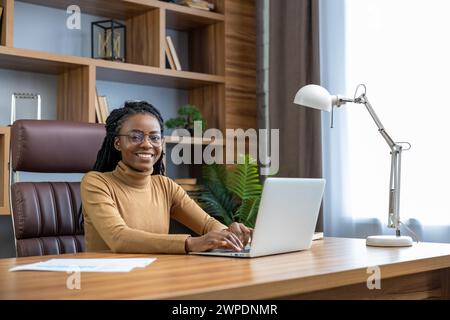 Una donna professionale allegra e sorridente lavora online da casa con un notebook Foto Stock