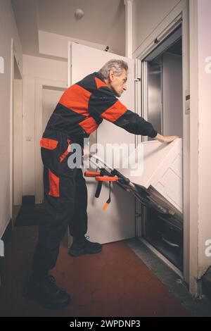 Un uomo anziano in generale che muove lavatrice su un carrello con ascensore Foto Stock