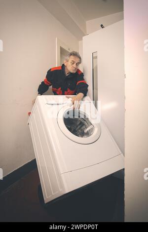 Un uomo anziano in generale che muove lavatrice su un carrello con ascensore Foto Stock
