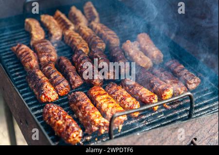 Piccoli involtini rumeni sminuzzati chiamati mici o mititei, simili ai cevapi serbi, salsicce fresche balcaniche senza pelle, cotte all'aperto sul barbecue Foto Stock