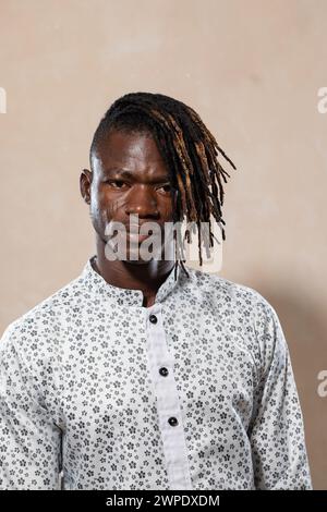 Giovane uomo rilassato con dreadlock in piedi su uno sfondo neutro in una camicia stampata che riflette lo stile moderno e la sicurezza casual Foto Stock