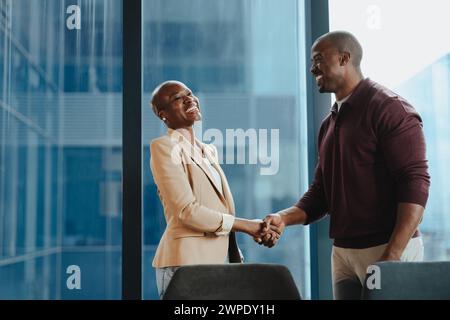 Una manager felice stringe la mano al suo collega dopo una riunione di promozione in una sala riunioni aziendale. Due uomini d'affari che celebrano un successfu Foto Stock