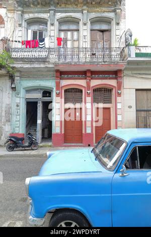 038 una vecchia auto classica blu parcheggiata di fronte alla facciata scheggiata di una casa con lavanderia sul balcone. L'Avana vecchia-Cuba. Foto Stock