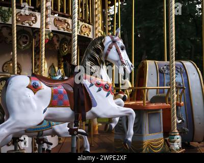 Primo piano di una figura a cavallo con pali e selle come posti a sedere in un tradizionale carosello colorato vecchio stile all'aperto. Divertimento vintage per tutta la famiglia. Foto Stock