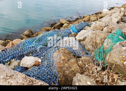 Immagine che mostra le reti da pesca scartate lavate su rocce nel porto che inquinano l'ambiente Foto Stock