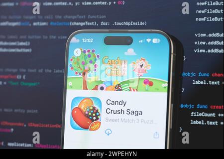 New York, USA - 23 febbraio 2024: Gioco T Candy Crush Saga su schermo iphone in background di programmazione codice sfocato Foto Stock