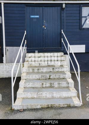 Gradini bianchi con corrimano che conducono alla cabina in legno dipinta di blu con doppia porta chiusa e cartello sulla porta che dice la cabina e la finestra sul lato della. Foto Stock