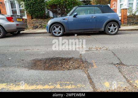 Grande pozzo in una strada a Westcliff on Sea, Southend, Essex, Regno Unito, che necessita di riparazione. Parcheggiate le auto vicino al buco Foto Stock