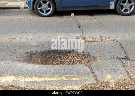 Grande pozzo in una strada a Westcliff on Sea, Southend, Essex, Regno Unito, che necessita di riparazione. Macchina parcheggiata presso il buco. Vedere l'immagine 2WPFXCG per la riparazione Foto Stock