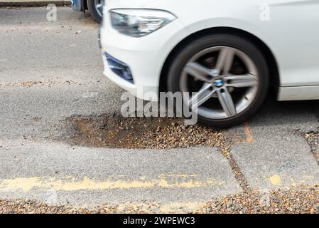 Grande pozzo in una strada a Westcliff on Sea, Essex, Regno Unito, che necessita di riparazione. L'auto sta per entrare nel buco Foto Stock