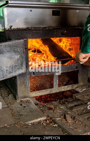 Stoking firebox sotto evaporatore con legno in sugarhouse lavorazione di sap d'acero in sciroppo in una fattoria Amish in Michigan, Stati Uniti [nessun rilascio di proprietà; modifica Foto Stock