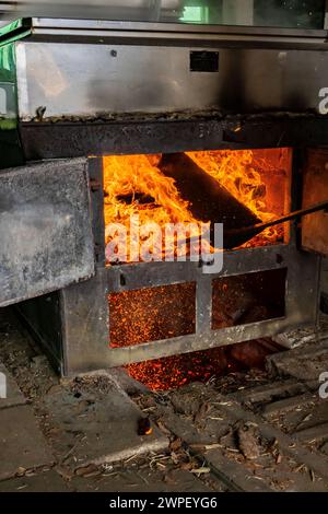 Stoking firebox sotto evaporatore con legno in sugarhouse lavorazione di sap d'acero in sciroppo in una fattoria Amish in Michigan, Stati Uniti [nessun rilascio di proprietà; modifica Foto Stock