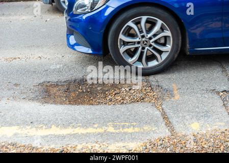 Grande pozzo in una strada a Westcliff on Sea, Southend, Essex, Regno Unito, che necessita di riparazione. La macchina passa per il buco Foto Stock