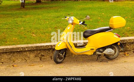 scooter giallo d'epoca parcheggiato sulla strada accanto a un parco. Foto Stock