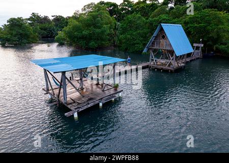 Un uomo, turista su un molo di legno vicino a un bellissimo cottage turistico sul mare in una baia isolata di San Cristobal isola di Bocas del Toro, Panama Foto Stock