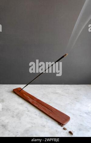 Il fumo prodotto dallo stick di incenso acceso si trova su un supporto per incenso. Foto Stock