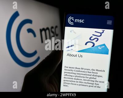 Persona che detiene un cellulare con pagina web dell'evento annuale Munich Security Conference (MSC) davanti al logo. Messa a fuoco al centro del display del telefono. Foto Stock