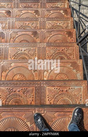 Antichi gradini in ghisa con ornamenti sulla strada della città. Scale in metallo vintage decorate con motivi eleganti all'aperto. Punto di riferimento storico Foto Stock
