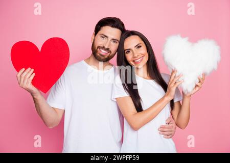 Ritratto fotografico di una giovane coppia con il cuore rosso, un soffice cuscino vestito con elegante indumento bianco, isolato su sfondo rosa Foto Stock