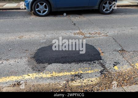 Grande pozzo riparato in una strada a Westcliff on Sea, Essex, Regno Unito, che necessita di riparazione. Auto parcheggiate con la riparazione di buchi. Vedere l'immagine 2WPEWC0 per il foro per buche Foto Stock