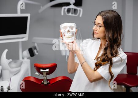 Ritratto del dentista femmina che tiene il modello del cranio e che spiega le regole di igiene dei denti al paziente presso la telecamera. Foto Stock