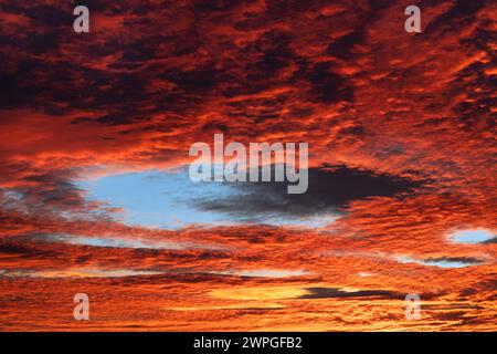 Paesaggio nuvoloso rosso con buco blu nelle nuvole cirrocumulative al crepuscolo serale. Un bellissimo bagliore di luce sul cielo arancione al tramonto con un'insolita cavum Foto Stock