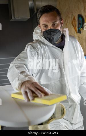 Produzione di tavole da surf, Shaper che lavora sui dettagli della tavola. Concetto di produzione industriale, professionale qualificata, professione e occupazione. Foto Stock