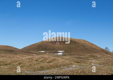 Tumulo sepolcrale ricoperto di erba in un paesaggio di cultura collinare ondulato. Macchie di neve a terra Foto Stock