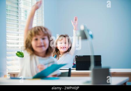 Carino piccoli alunni che alzano le mani durante la lezione. Bambini in classe a scuola. Foto Stock