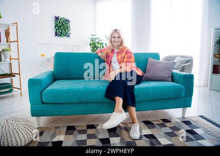 Foto di una donna allegra e anziana seduto a un divan sorridente goditi l'acquisto di una nuova casa al chiuso Foto Stock