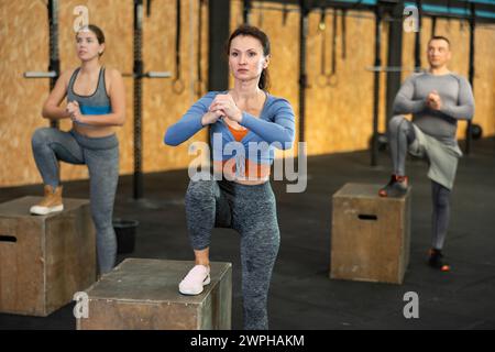 La donna esegue esercizi di squat, arrampicata in collina, squat kettlebell utilizzando la piattaforma fitness e il cubo Foto Stock