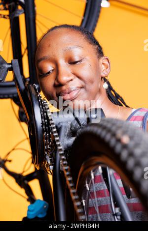 Vista dettagliata della donna nera che esamina attentamente il supporto della catena per una bicicletta ottimale. La giovane donna in primo piano mostra la sua attenzione ai dettagli mentre cura diligentemente i componenti della sua moto. Foto Stock