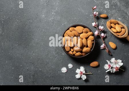 Mandorle dolci crude fresche in ciotola di legno o pala con fiori di mandorle su sfondo rustico, noci, cibo sano Foto Stock