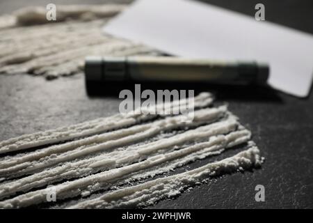 Tossicodipendenza. Banconota da cocaina e dollaro arrotolato su un tavolo con texture scura, primo piano Foto Stock