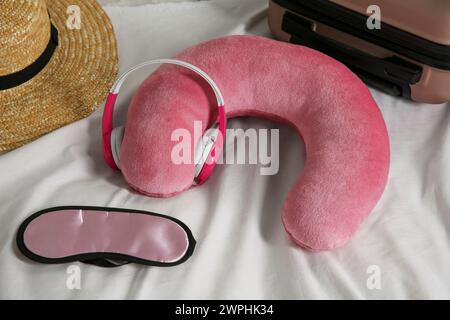 Cuscino da viaggio rosa con cuffie, valigia, cappello e maschera dormiente sul letto Foto Stock