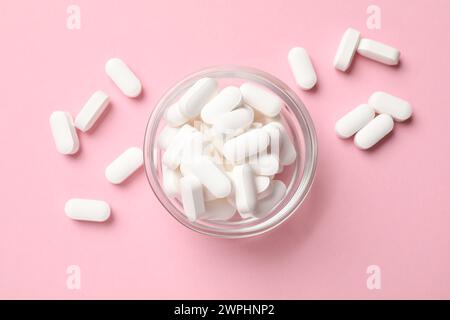 Capsule vitaminiche nel recipiente su sfondo rosa, vista dall'alto Foto Stock