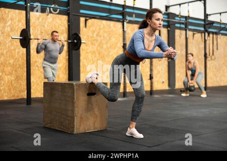 La donna esegue esercizi di squat, arrampicata in collina, squat kettlebell utilizzando la piattaforma fitness e il cubo Foto Stock