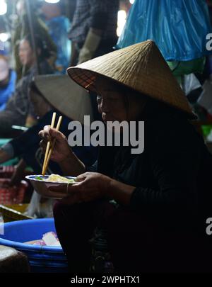 Una donna vietnamita che mangia una ciotola di spaghetti per colazione al mercato del pesce fresco e del pesce di mattina presto a Thanh Hà, Hoi An, Vietnam. Foto Stock