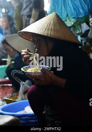 Una donna vietnamita che mangia una ciotola di spaghetti per colazione al mercato del pesce fresco e del pesce di mattina presto a Thanh Hà, Hoi An, Vietnam. Foto Stock