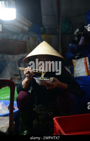 Una donna vietnamita che mangia una ciotola di spaghetti per colazione al mercato del pesce fresco e del pesce di mattina presto a Thanh Hà, Hoi An, Vietnam. Foto Stock