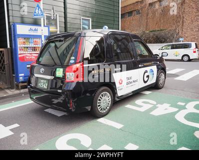 TOKYO, GIAPPONE - 7 marzo 2024: Un taxi passa davanti a un distributore automatico di bevande in una strada nella zona Yayoi di Tokyo nel Bunkyo Ward. Foto Stock