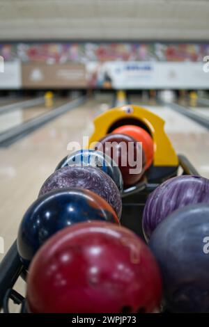 Palline da bowling colorate in una macchina di ritorno presso la pista da bowling. Corsie e spille su sfondo sfocato. Foto Stock