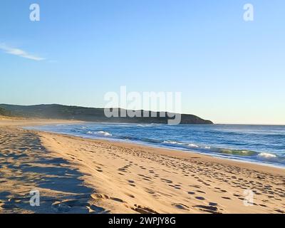 Una spiaggia sabbiosa con orme e dolci onde che lambiscono la riva Foto Stock