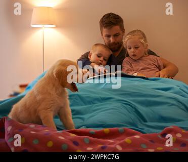 Cani, bambini o padre che leggono libri a letto per imparare, educare o raccontare storie a casa di notte. Famiglia, relax o papà con bambini fratelli per un Foto Stock