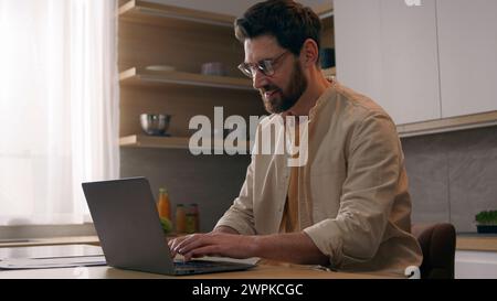 Un uomo d'affari in cucina considera un giornalista che lavora su un notebook alla ricerca di ispirazione e nuove idee per il libero professionista autore di articoli Foto Stock