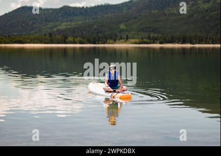 Ragazzo in paddleboard nel tranquillo lago di montagna Foto Stock
