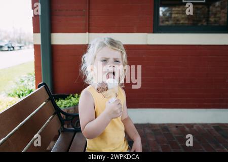 Un bambino che lecca il cono di gelato nella piazza della città Foto Stock