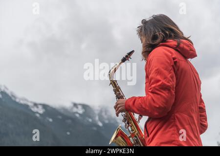 Donna che suona il sassofono in montagna con spartiti musicali Foto Stock