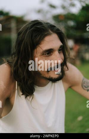Ritratto di un giovane sorridente con lunghi capelli castani e occhi scuri. Foto Stock